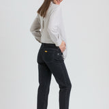 A woman wearing dark wash slim-fit jeans, a light gray and white vertically striped long-sleeve shirt, and black flats, shown from a side-back angle against a light gray studio background.