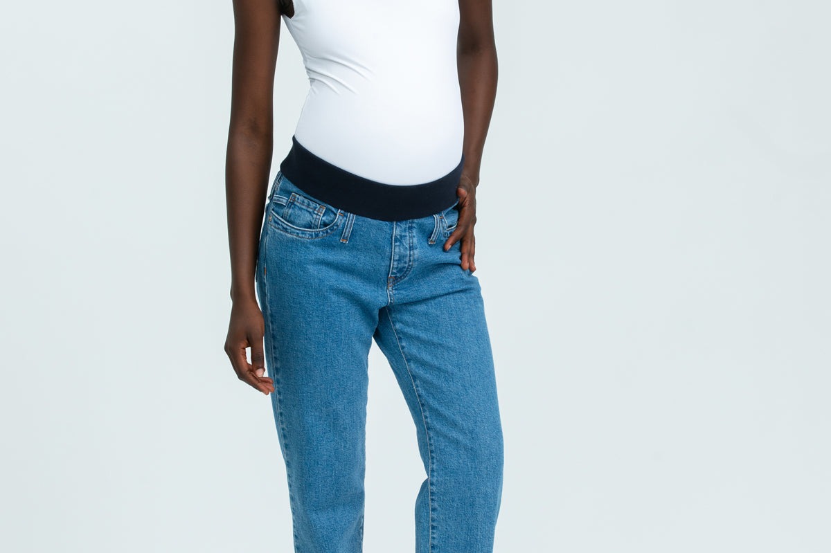 Woman wearing blue maternity jeans and white vest top