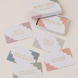 A boxed set of affirmation cards arranged on a light cream background. The white box is labeled 'MIND CARDS AFFIRMATIONS FOR EIGHTH' and one card is pulled out reading 'STRENGTH.