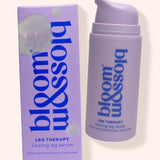 A lavender pump bottle and matching box of bloom blossom leg therapy cooling leg serum on a light beige background.