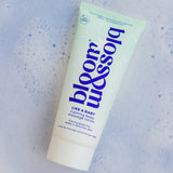 A squeeze tube of blossom baby massage lotion on a light blue textured background with small blue speckles. The tube is pale mint green with dark blue text and a white cap.