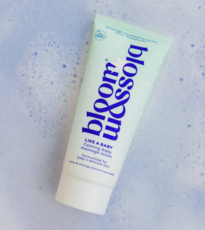 A squeeze tube of blossom baby massage lotion on a light blue textured background with small blue speckles. The tube is pale mint green with dark blue text and a white cap.