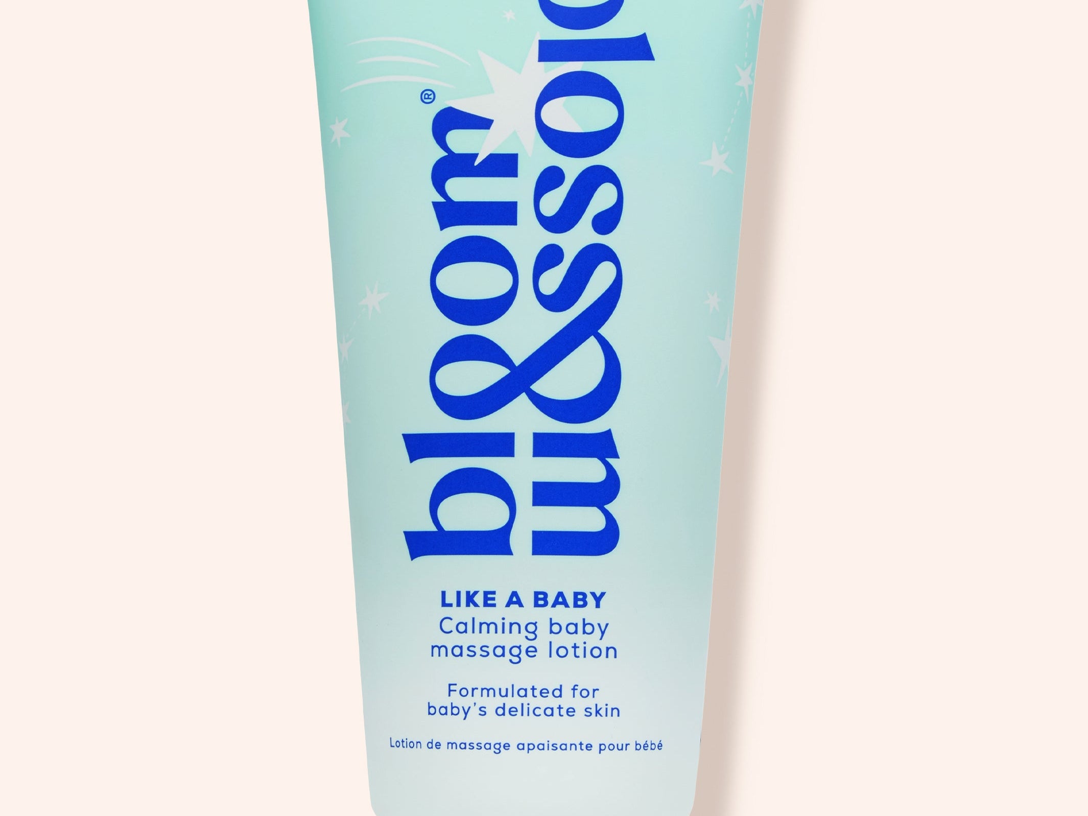 A light blue squeeze tube of bloom & blossom 'Like a Baby' calming baby massage lotion, set against a solid pale peach background.