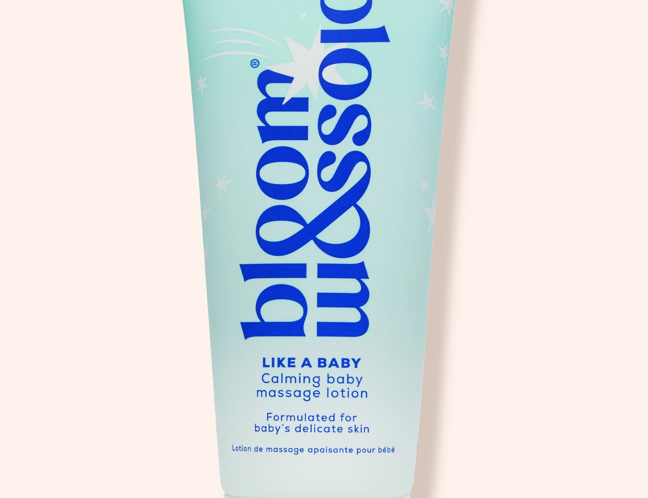 A light blue squeeze tube of bloom & blossom 'Like a Baby' calming baby massage lotion, set against a solid pale peach background.