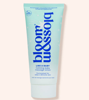 A light blue squeeze tube of bloom & blossom 'Like a Baby' calming baby massage lotion, set against a solid pale peach background.