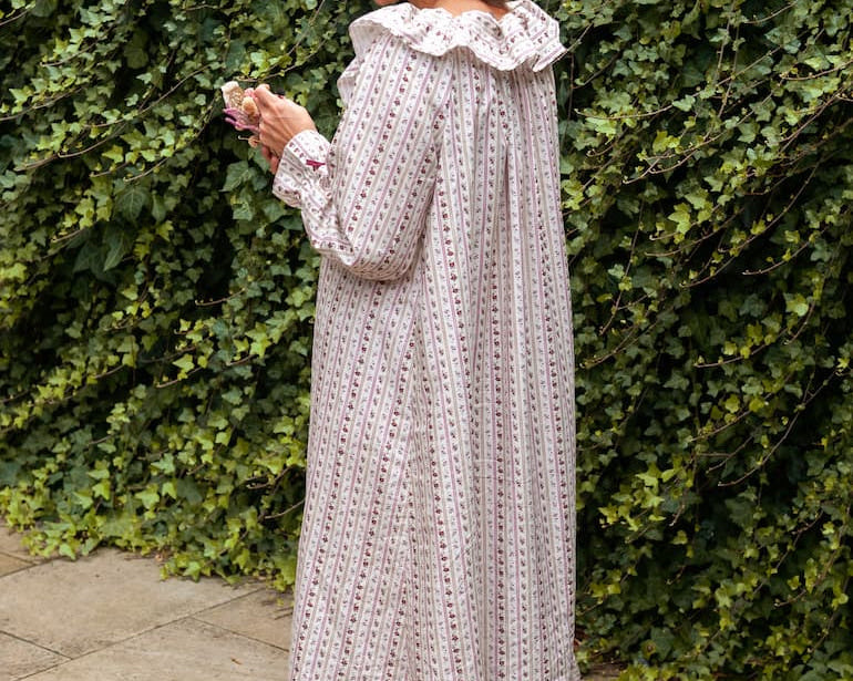 Beatrice Rose Stripe nightie back view on a woman by an ivy wall, showing the ruffled collar and tiered hem