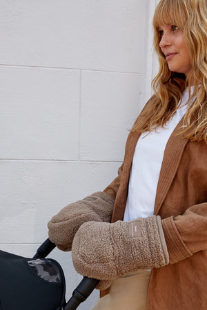 Astrid Eco stroller mittens in Mocha Borg on a woman in a tan jacket pushing a pram and looking to the side