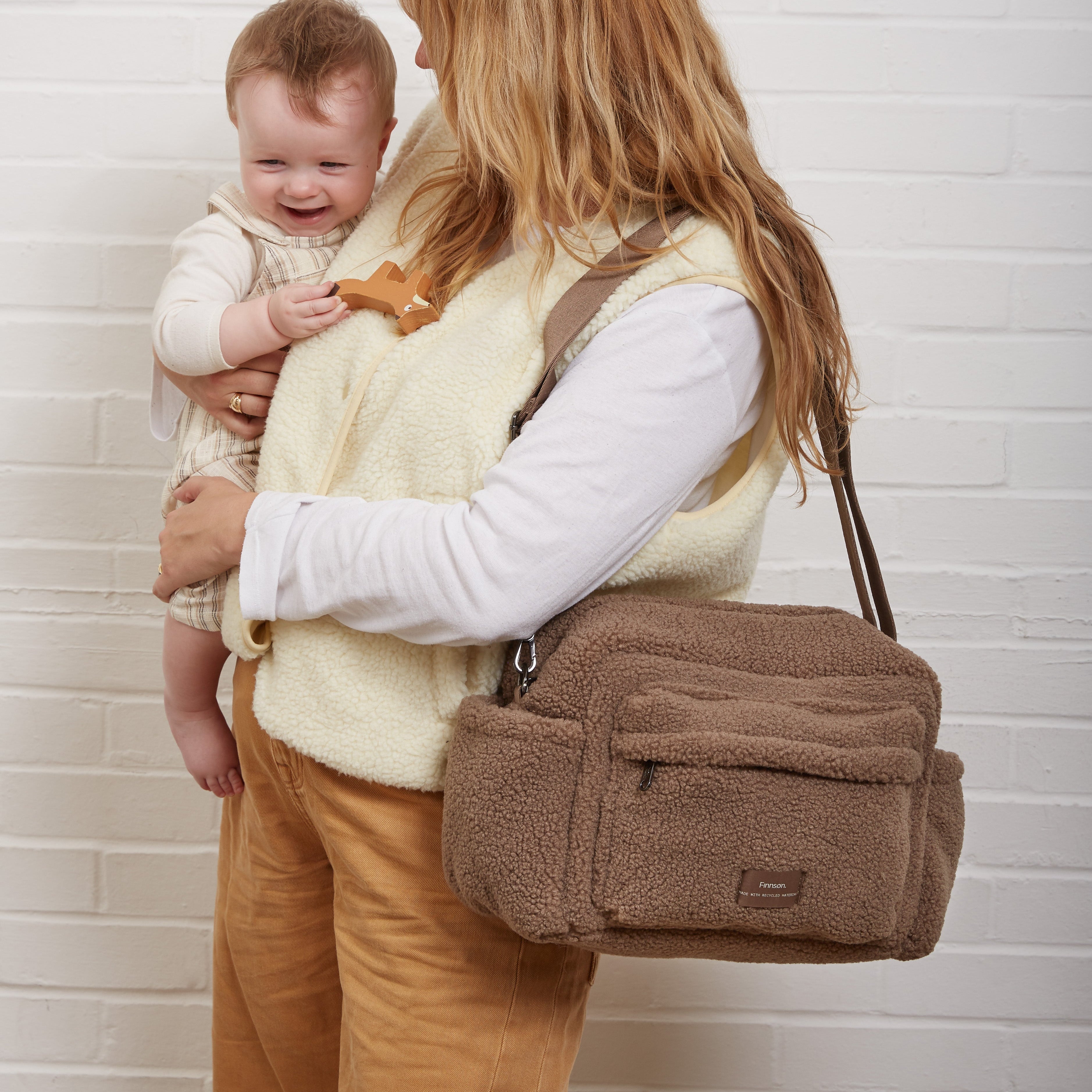 Freya Eco Stroller Organiser in Mocha Borg worn crossbody by a woman while she holds a smiling baby