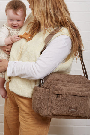 Freya Eco Stroller Organiser in Mocha Borg worn crossbody by a woman while she holds a smiling baby