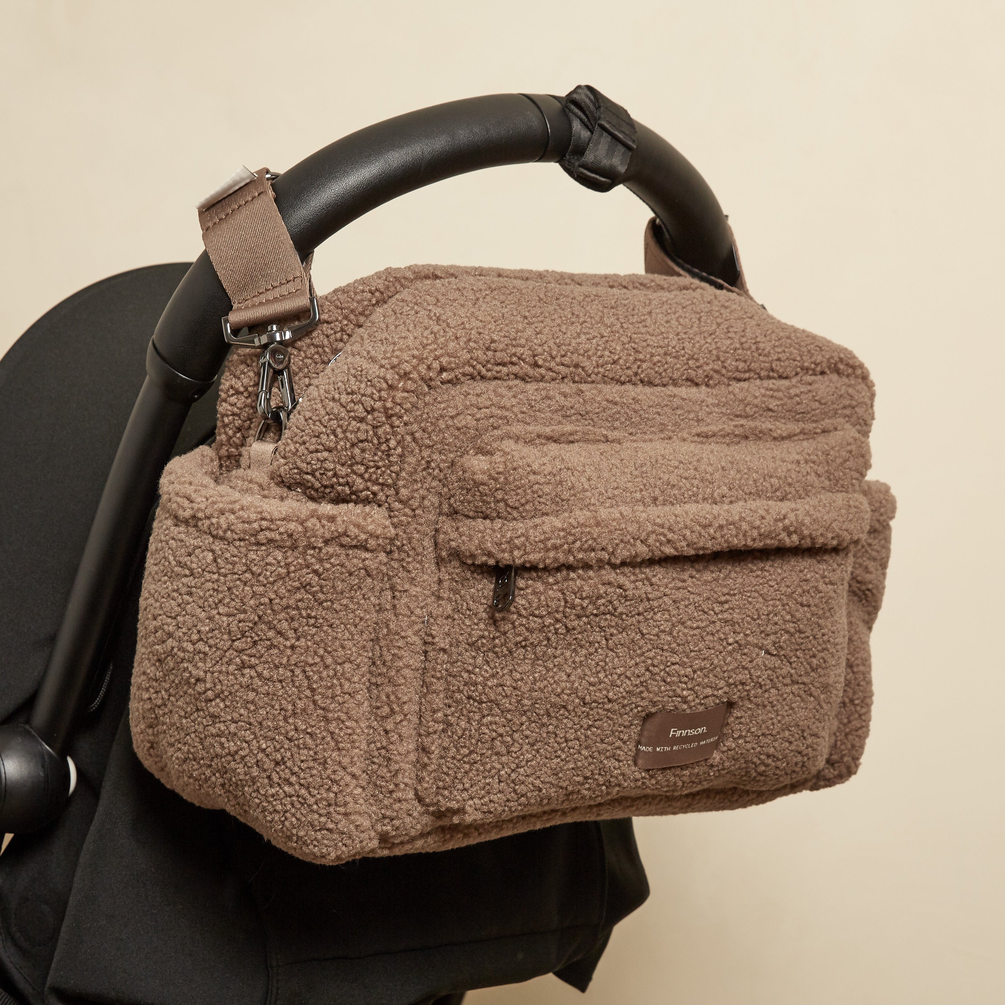 Freya Eco Stroller Organiser in Mocha Borg hanging from the black handlebar of a pushchair, front pocket facing out