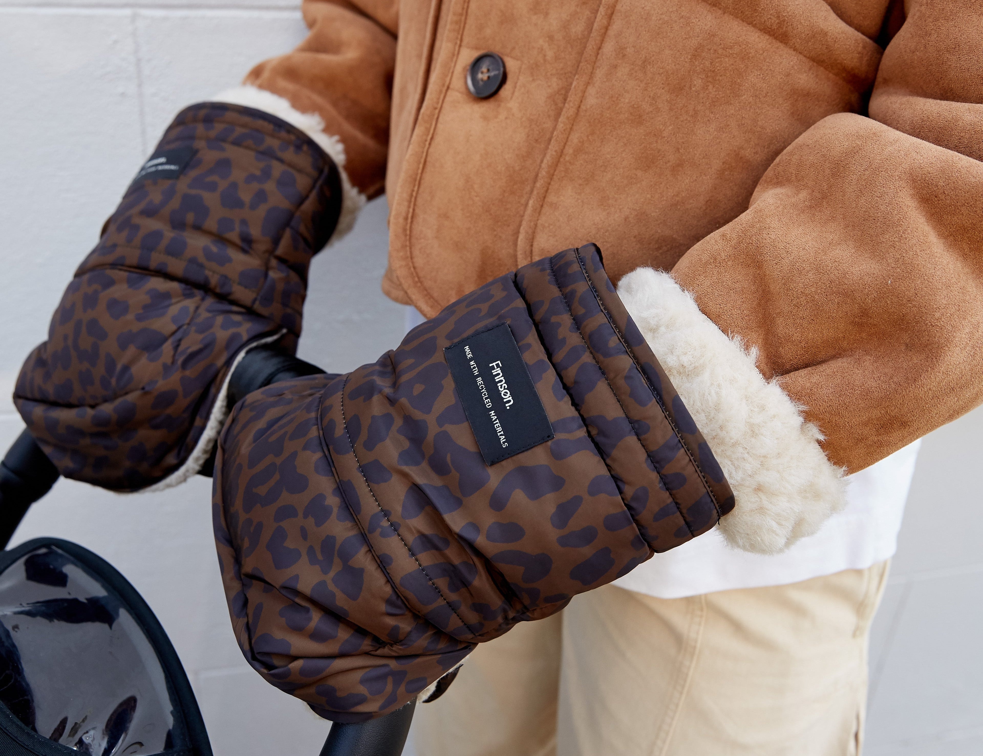 Woman wearing the Astrid stroller mittens in Chocolate Leopard on a stroller handle, with cream fleece cuffs
