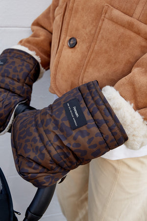 Woman wearing the Astrid stroller mittens in Chocolate Leopard on a stroller handle, with cream fleece cuffs