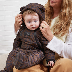 ANDERS Eco Snowsuit Chocolate Leopard worn by a baby sitting on a woman's lap while she adjusts the hood