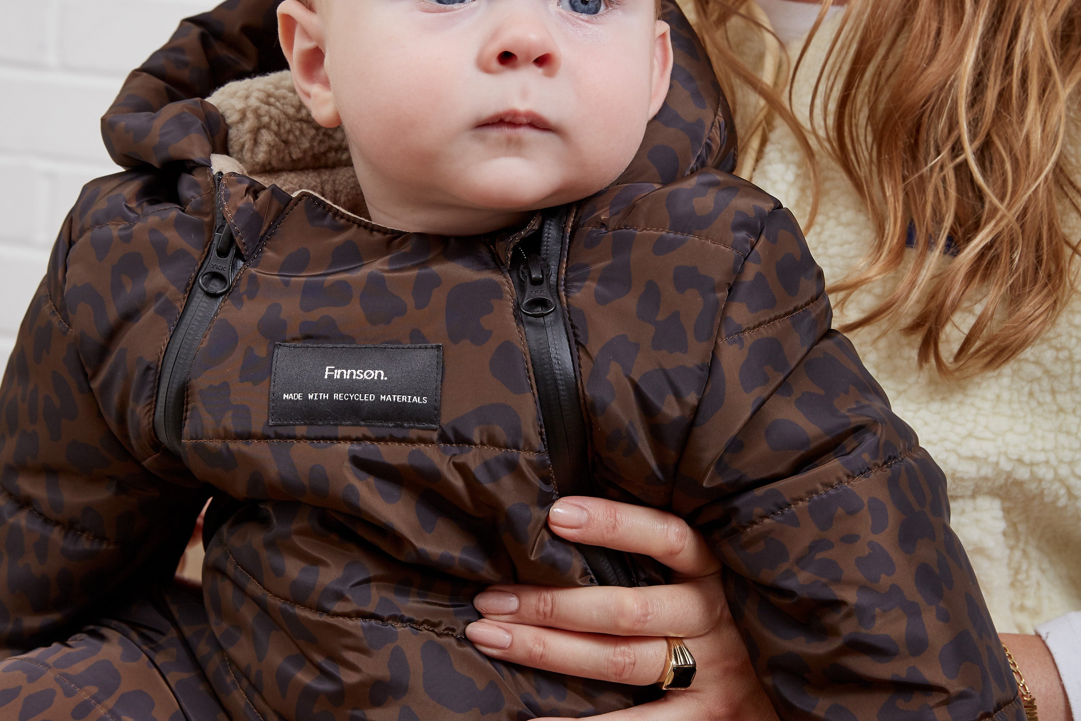 ANDERS Eco Snowsuit Chocolate Leopard close-up of a baby wearing it, showing the front zips and Finnson label