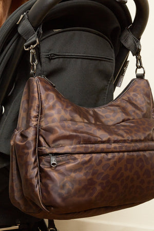 Clara Eco Changing Bag, Chocolate Leopard, hanging from the handlebar of a black pram on clips
