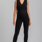 Woman wearing a black sleeveless top and leggings on a gray background