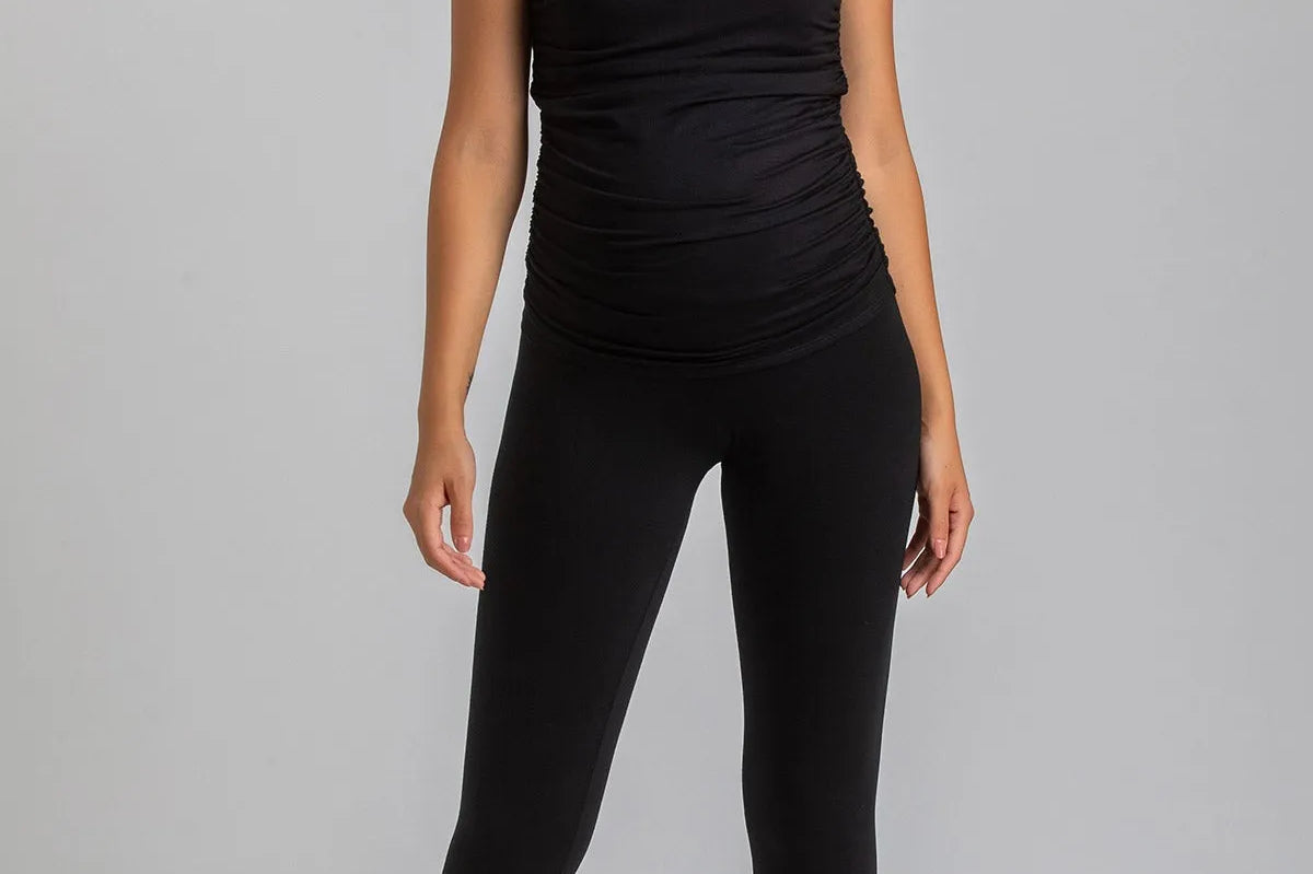 Woman wearing a black sleeveless top and leggings on a gray background