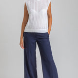 Woman wearing a white sleeveless top and navy pants on a gray background