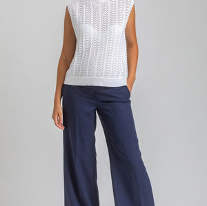 Woman wearing a white sleeveless top and navy pants on a gray background