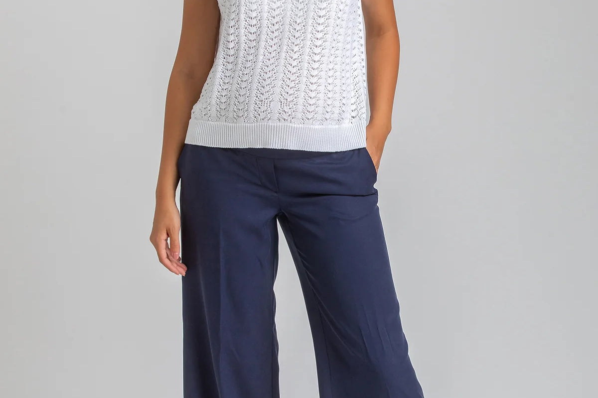 Woman wearing a white sleeveless top and navy pants on a gray background