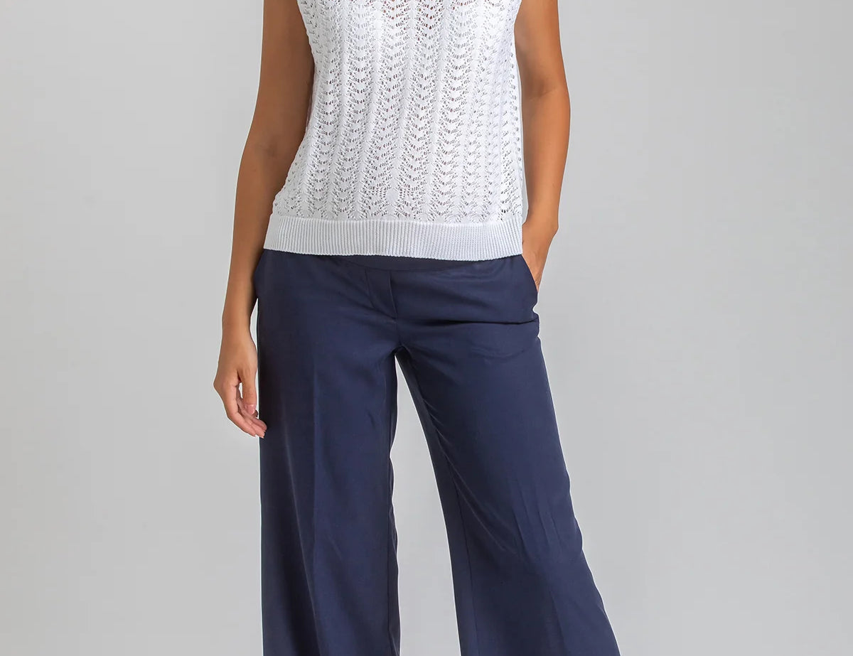 Woman wearing a white sleeveless top and navy pants on a gray background