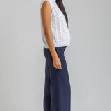 Woman wearing a white sleeveless top and navy pants on a gray background