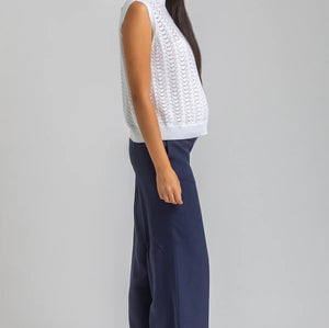 Woman wearing a white sleeveless top and navy pants on a gray background