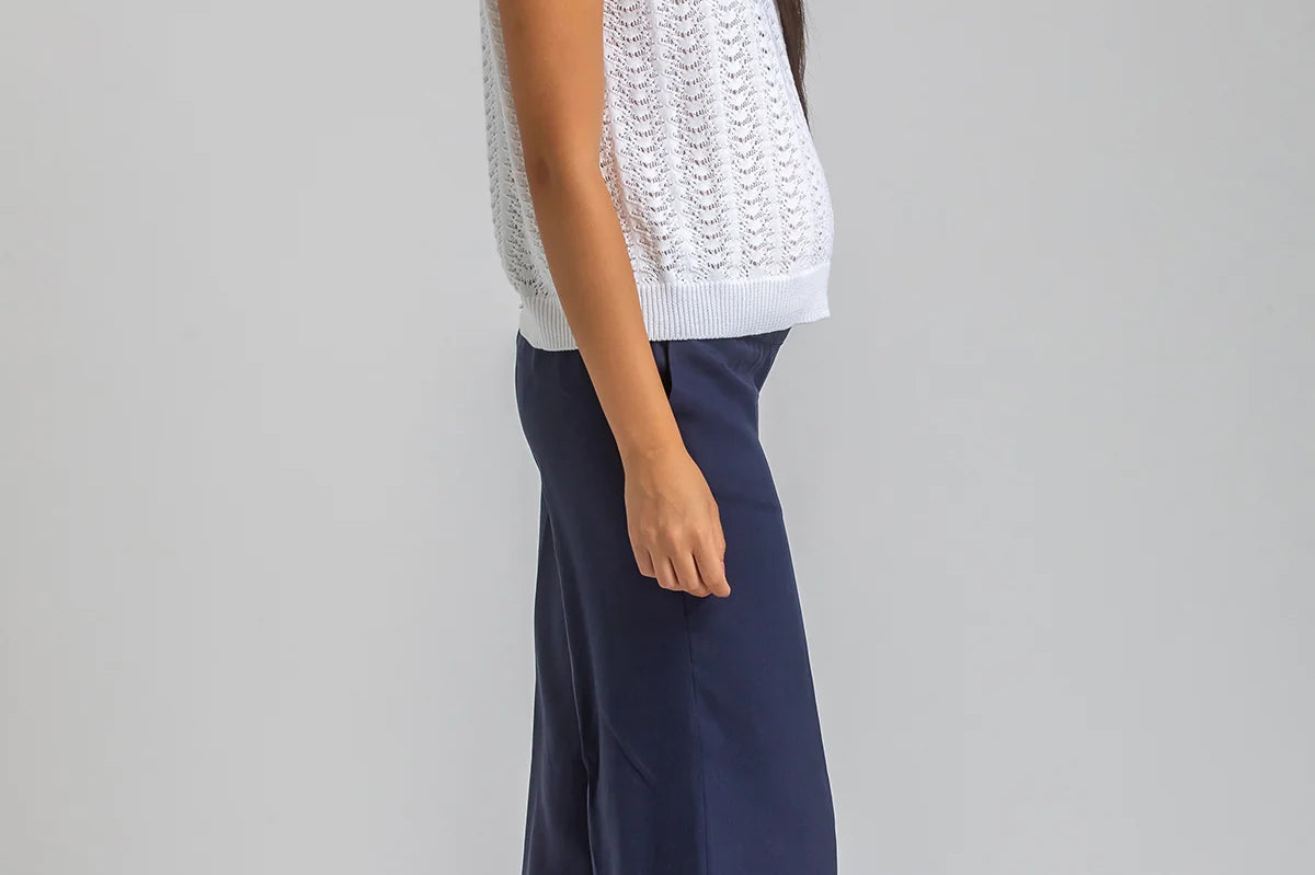 Woman wearing a white sleeveless top and navy pants on a gray background