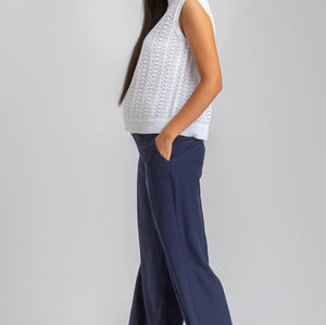 Woman wearing a white sleeveless top and navy pants on a plain background