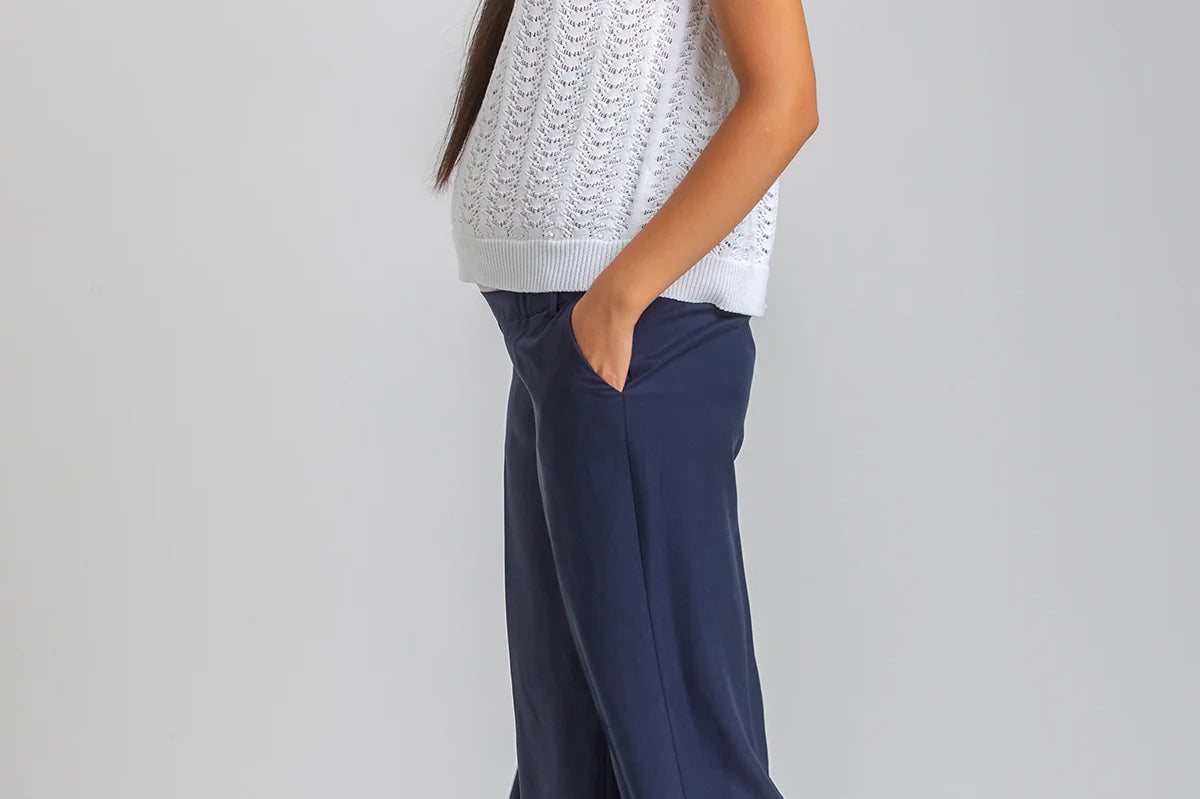 Woman wearing a white sleeveless top and navy pants on a plain background