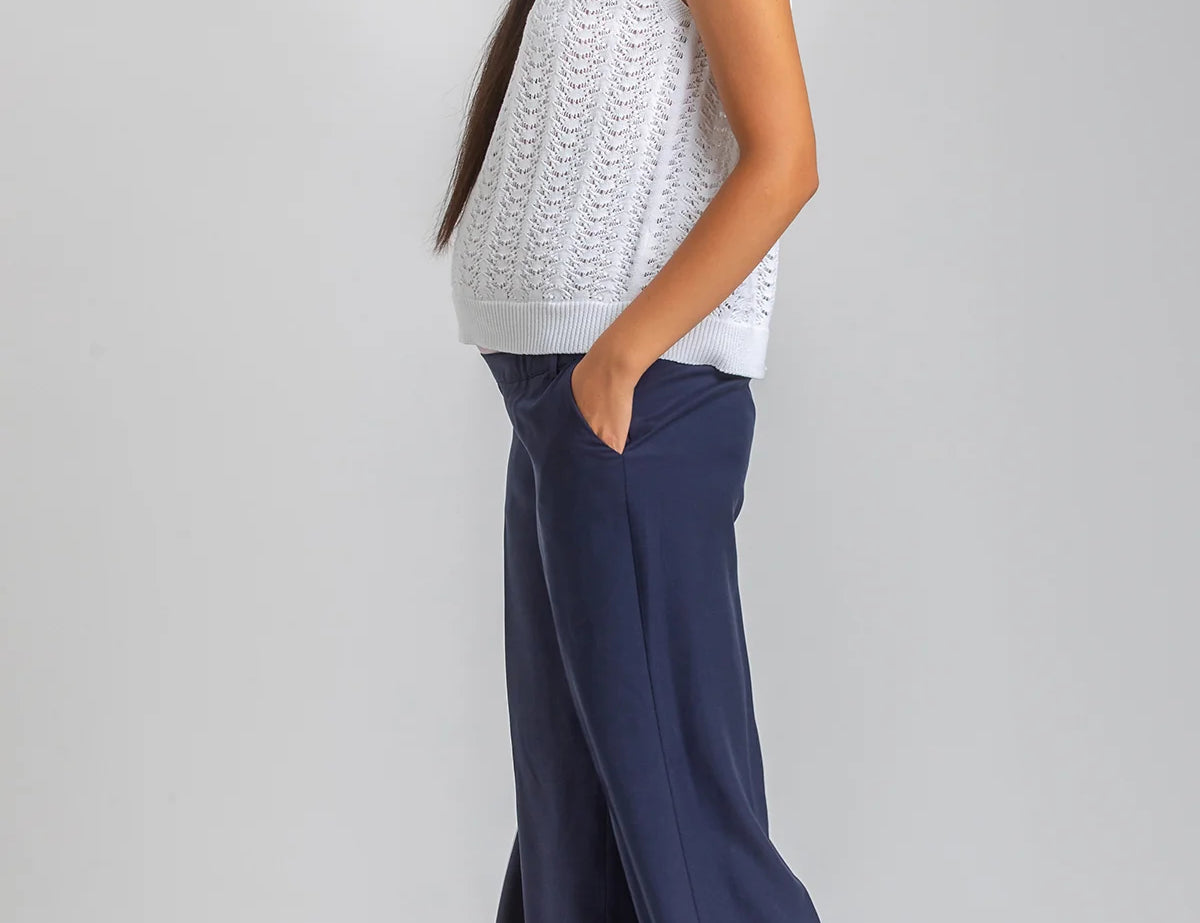 Woman wearing a white sleeveless top and navy pants on a plain background