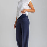 Woman wearing a white sleeveless top and navy pants on a gray background