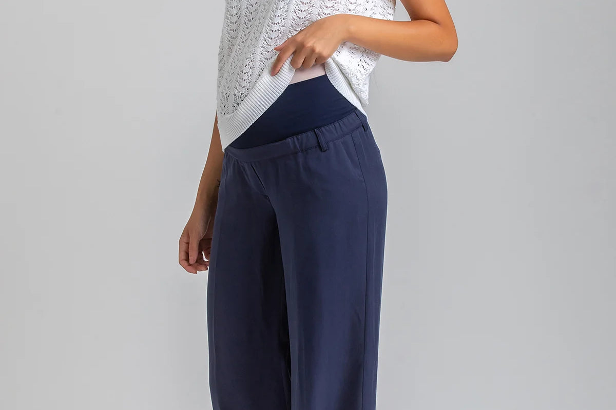 Woman wearing a white sleeveless top and navy pants on a gray background