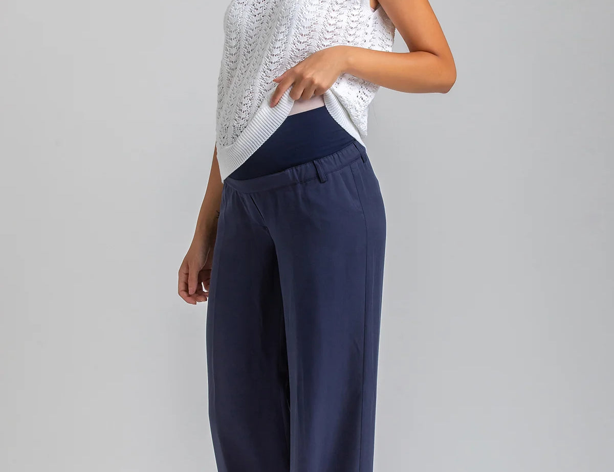 Woman wearing a white sleeveless top and navy pants on a gray background