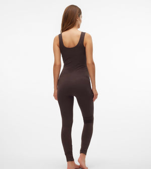 A woman viewed from behind wearing a dark brown sleeveless bodysuit and matching leggings against a plain white studio background.