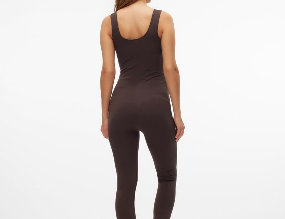 A woman viewed from behind wearing a dark brown sleeveless bodysuit and matching leggings against a plain white studio background.