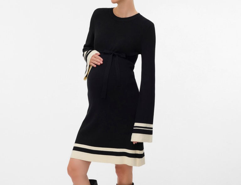 Pregnan woman wear black knitted dress that is above the knee, with long sleeves. The dress is black with ivory stripes on the hem and sleeves.