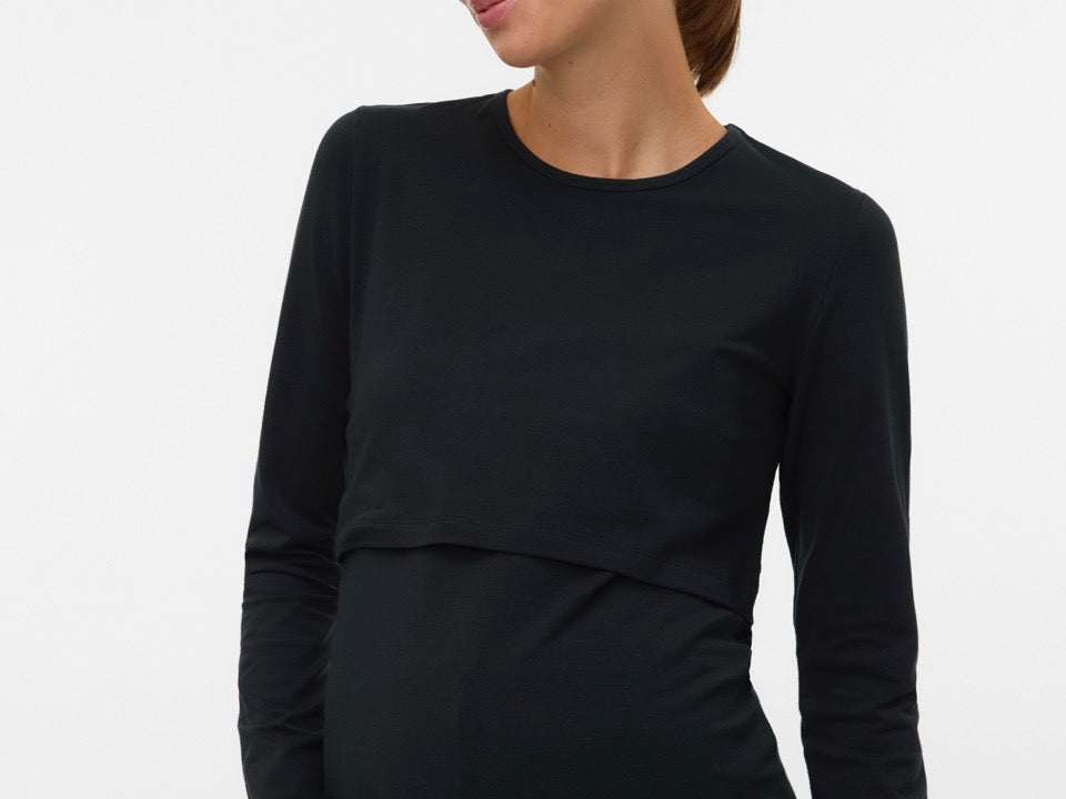 A pregnant woman wearing a black long-sleeve maternity top with a layered underbust design, shown against a plain light gray studio background.