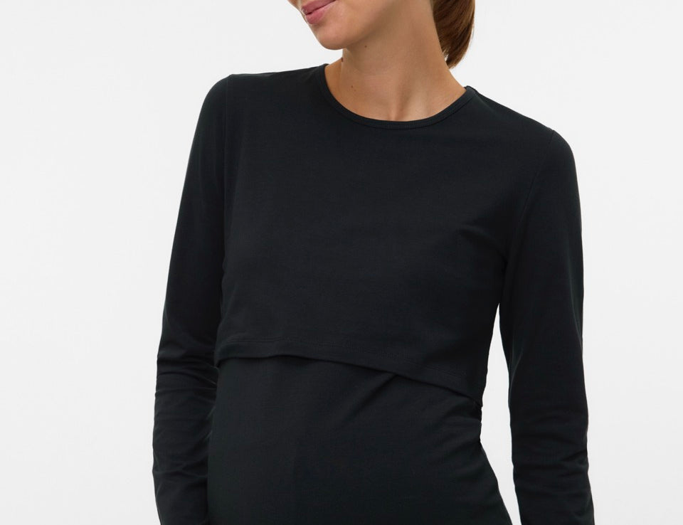 A pregnant woman wearing a black long-sleeve maternity top with a layered underbust design, shown against a plain light gray studio background.