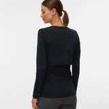 A woman shown from the back wearing a black long-sleeve cropped top and dark gray pants, photographed against a plain light gray studio background.
