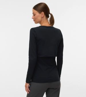 A woman shown from the back wearing a black long-sleeve cropped top and dark gray pants, photographed against a plain light gray studio background.