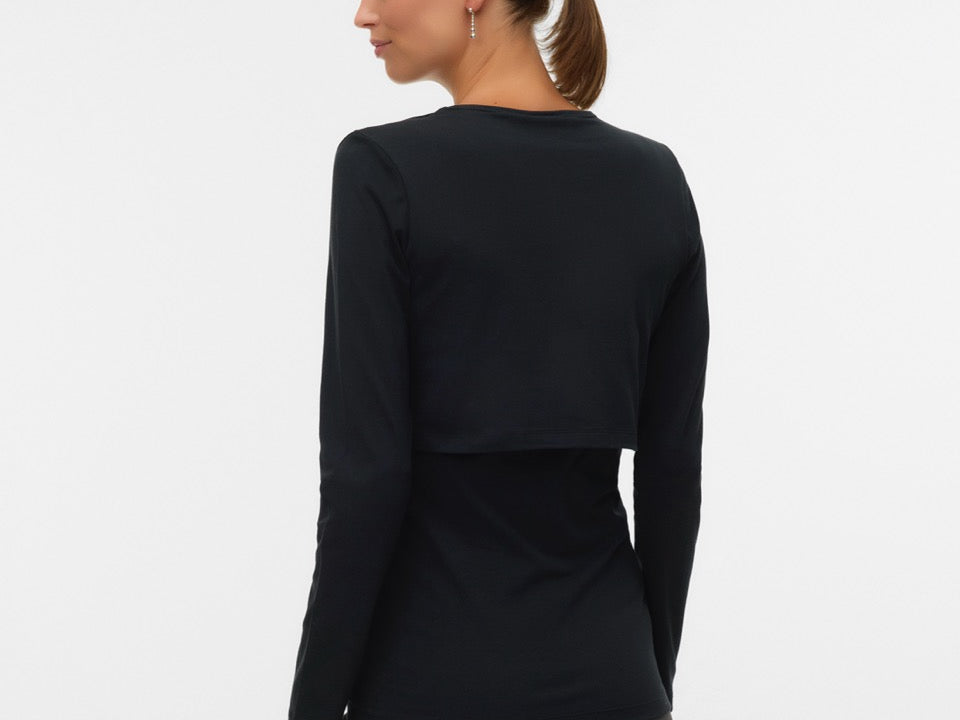 A woman shown from the back wearing a black long-sleeve cropped top and dark gray pants, photographed against a plain light gray studio background.