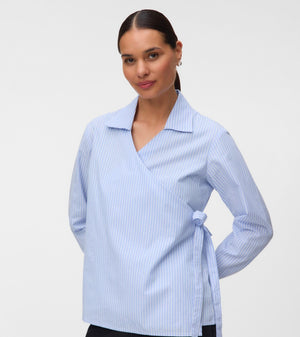 A woman modeling a light blue and white vertically striped wrap blouse with a collar and side tie, paired with black trousers, against a plain light gray studio background.