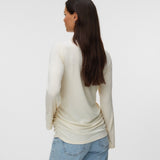 A woman with long dark brown hair is shown from the back wearing a cream-colored long-sleeve knit top and light blue jeans against a plain light gray studio background.