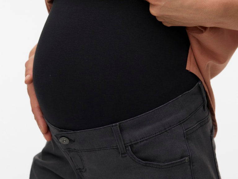 Person wearing a black maternity shirt and gray pants on a white background