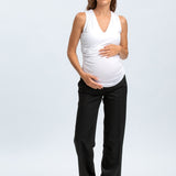 Pregnant woman wearing a white sleeveless top and black pants on a white background