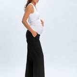 Pregnant woman wearing a white tank top and black wide-leg pants on a white background