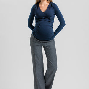 A woman modeling a dark navy blue long-sleeve V-neck top paired with gray wide-leg trousers and black heels, standing against a light gray studio background.