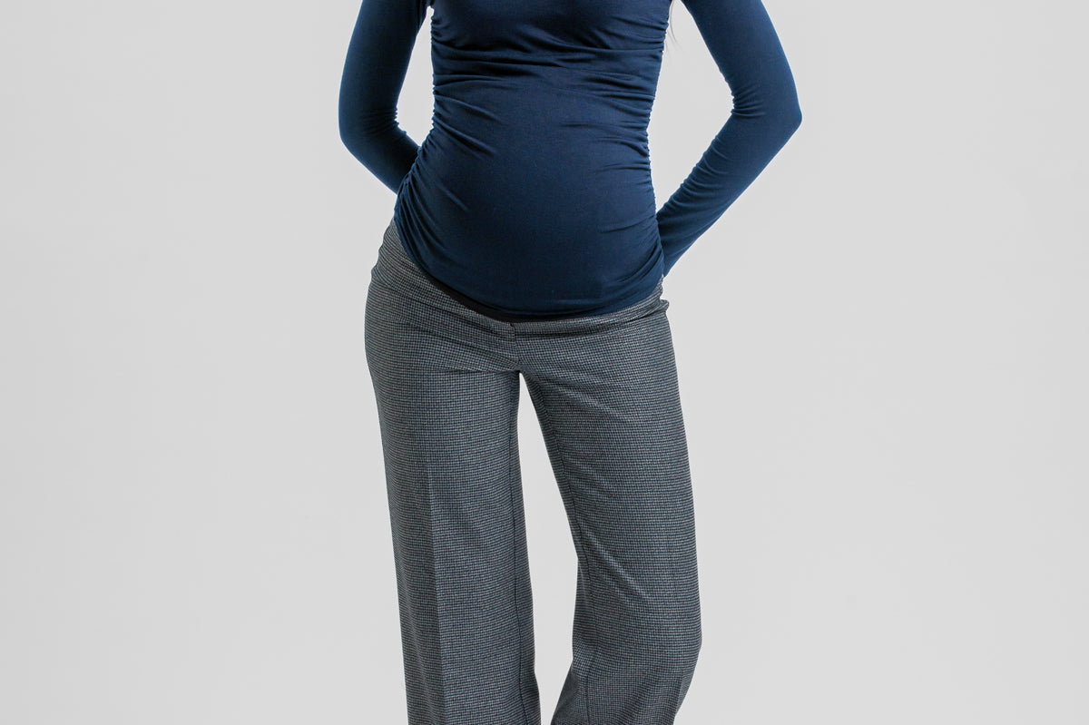 A woman modeling a dark navy blue long-sleeve V-neck top paired with gray wide-leg trousers and black heels, standing against a light gray studio background.