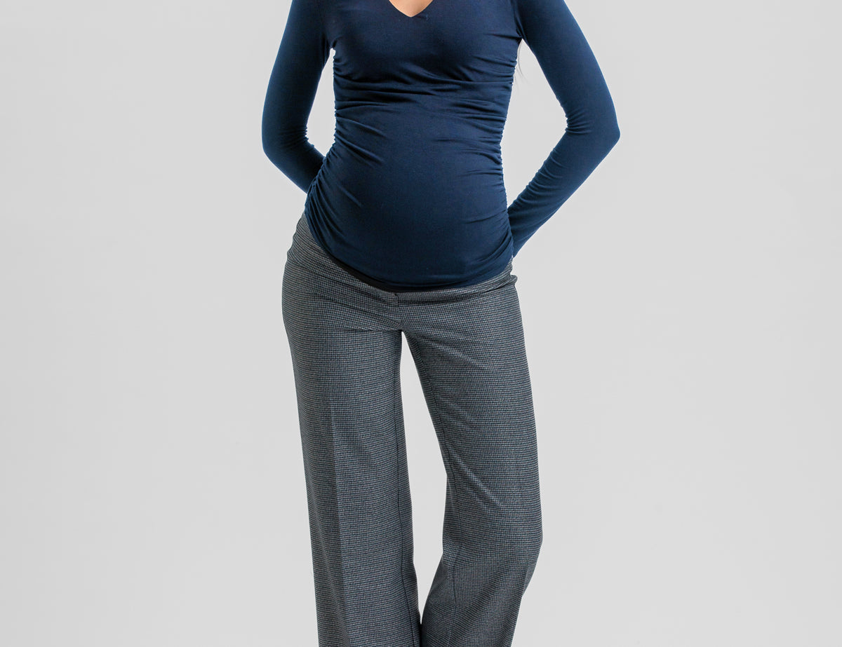 A woman modeling a dark navy blue long-sleeve V-neck top paired with gray wide-leg trousers and black heels, standing against a light gray studio background.